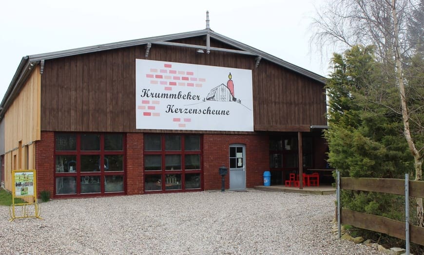 Außenansicht der Krummbeker Kerzenscheune: Scheune mit Holzfassade, roten Ziegeln und großem Schild