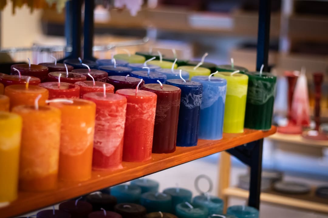 Stumpenkerzen in Gelb, Orange, Rot, Blau und Grün nebeneinander auf einem Holzregal